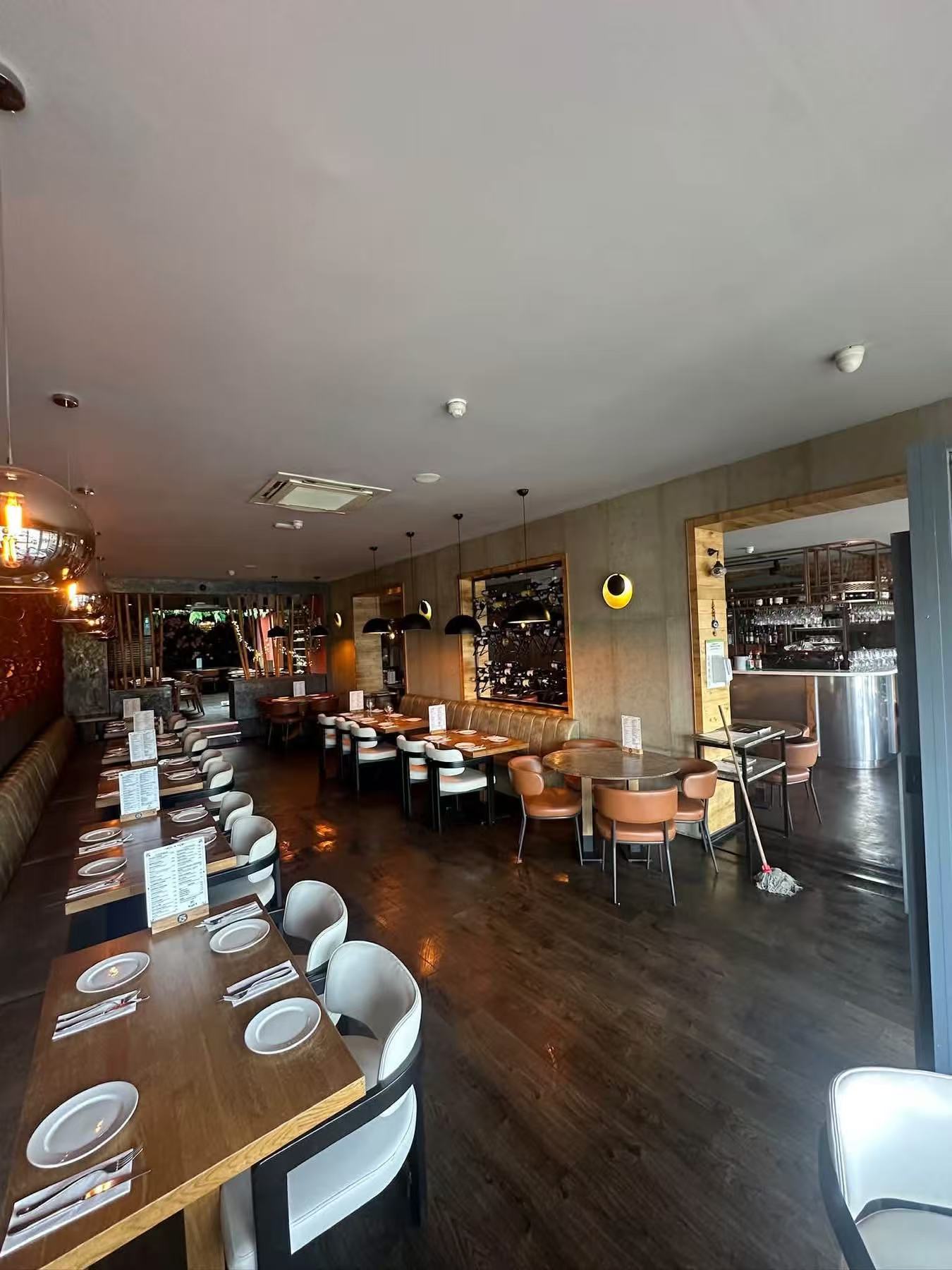 Restaurant interior showing a long dining table, mixed chairs, wall seating and bar access