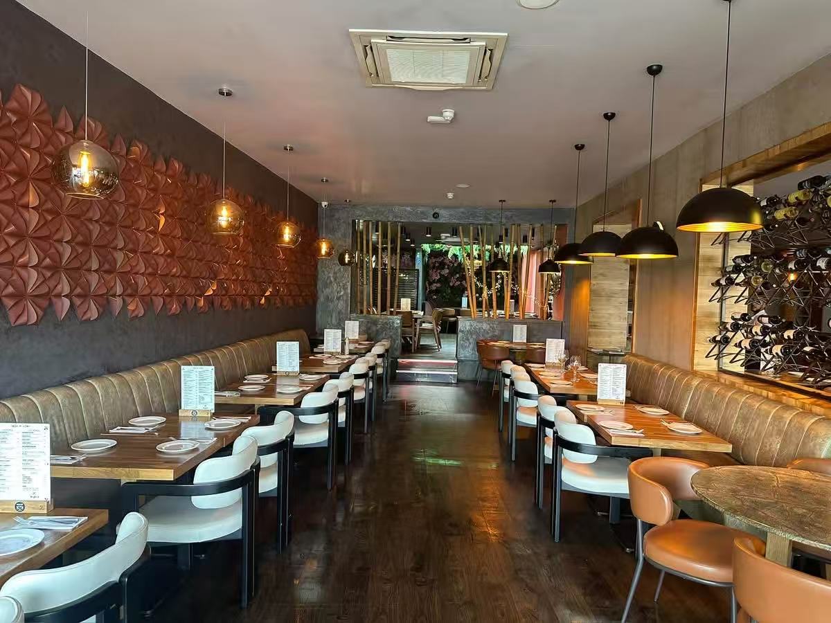 Long restaurant aisle framed by paired dining tables, upholstered chairs and banquette seating