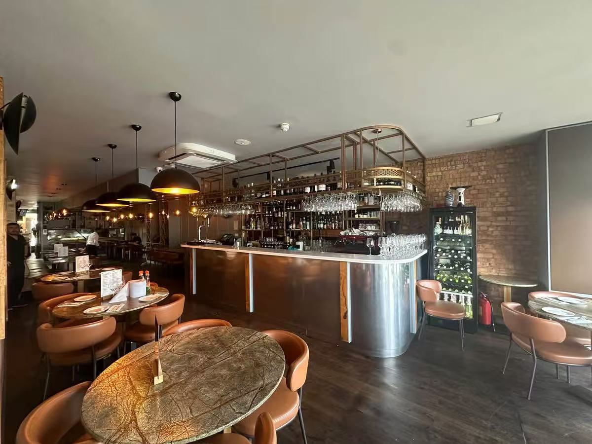 Restaurant bar area with metallic counter, pendant lights and round dining tables